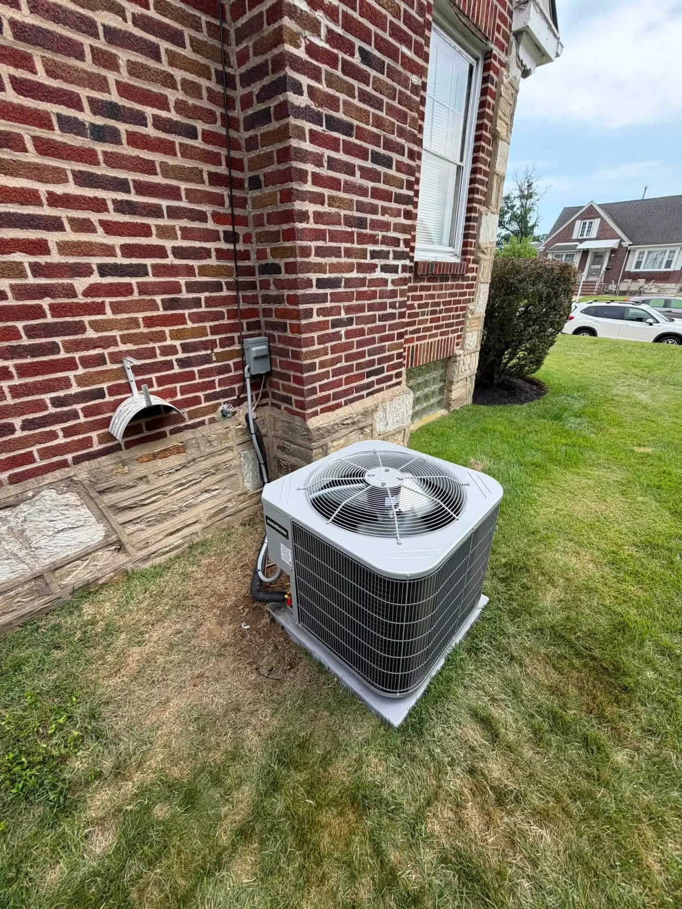 Outdoor residential HVAC condenser beside a brick home